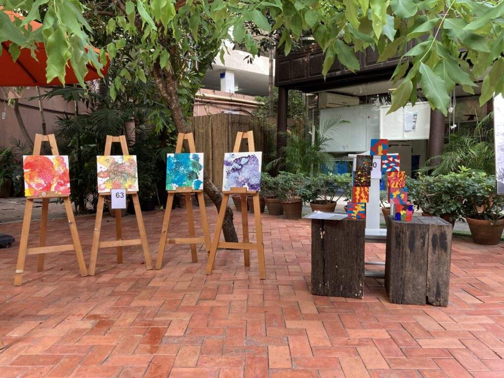 Collaborative paintings displayed on wooden easels in a school courtyard