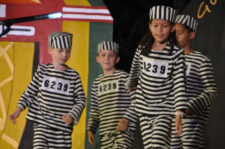 Children in striped costumes performing a dance number together on stage